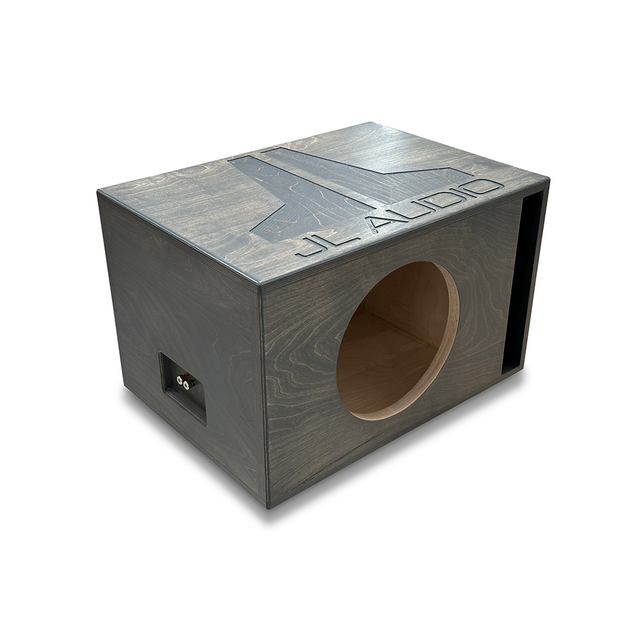 Angled view of a custom JL Audio single 12-inch W7 subwoofer enclosure featuring a sleek gray-stained Baltic Birch finish. The top panel showcases a large CNC-engraved JL Audio logo, adding a premium visual touch. The front baffle includes a precision-cut subwoofer opening and a tall, narrow slot port on the right side for deep, accurate bass response. A pre-wired spring terminal is installed on the left side panel for easy subwoofer connection. This enclosure combines high-performance tuning with stylish c